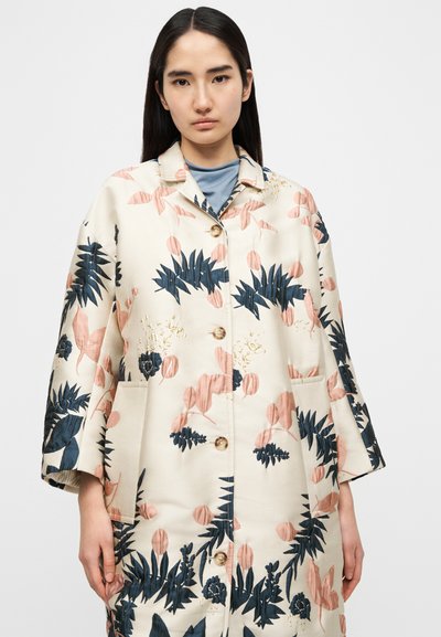 Manteau à motif floral ivoire, avec de grandes feuilles bleu foncé et pêche, un col à revers et des boutons dorés, doté de poches latérales.