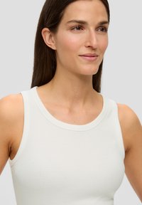 Canotta leggera bianca senza maniche con una texture a costine, scollatura rotonda e una leggera elasticità. Esibita su uno sfondo neutro.
