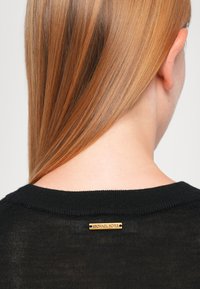 Zwarte gebreide trui met een ronde hals. Voorzien van een kleine gouden "Michael Kors" logo plaat op de achterkant, textiel met structuur, en een eenvoudig ontwerp.