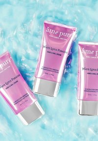 Drei Tuben Hand- und Nagelcreme, rosa Verpackung mit silbernen Akzenten, beschriftet mit "White Lotus Paradise", vor einem hellblauen Hintergrund.