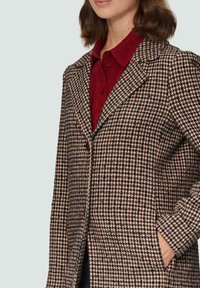Kariertes Tweed-Mantel mit Reverskragen, Vorderknöpfen und Seitentaschen, in einer Mischung aus Creme-, Schwarz- und Bordeauxtönen.