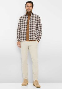 Camicia a quadri in marrone, bianco e blu; dolcevita beige sotto; pantaloni beige chiaro; sneaker casual color sabbia; texture del tessuto liscia.