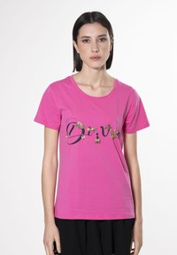 Camiseta de algodón rosa con mangas cortas, que presenta un texto en negro y adornos dorados en la parte delantera. Cuello redondeado, corte relajado.