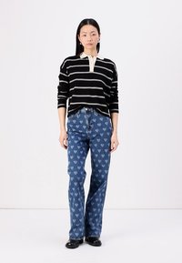 Črna prugasta pulover s kremasto ovratnikom, v kombinaciji z modrimi kavbojkami s svetlomodrim vzorcem srčkov, obut v črne čevlje.