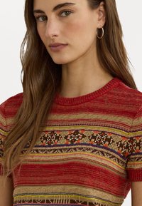 Pull en tricot à manches courtes, rayures texturées rouge et beige, motifs géométriques marron, orange et violet, encolure ronde.
