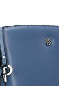 Blauwe leren handtas met een gladde textuur, voorzien van een zilveren logo-accent en een metalen ritssluiting in de vorm van de letter "P".