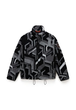 Giacca in pile nera e grigia con motivi geometrici; presenta un colletto alto, chiusura con zipper, tasche laterali e cordini regolabili.