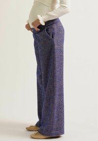Weite Hosen in einem lila Fischgrätenmuster, mit hoher Taille, seitlichen Taschen und lockerer Passform, kombiniert mit beigen Ballerinas.