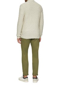 Helle beigefarbene gesteppte Sweater mit hohem Kragen, kombiniert mit olivgrünen, taillierten Hosen und weißen Sneakers mit marineblauen Akzenten.
