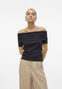 Svart av-shoulder topp, korte ermer, glatt tekstur. Kombinert med beige høytliv bukser, strukturert design med folder.
