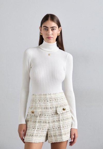 Witte geribde coltrui gecombineerd met textuurlijke beige short met gouden knoopaccenten en zijzakken. Schoon ontwerp, aansluitende silhouet.