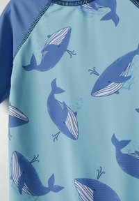 Tissu de maillot de bain bleu clair avec un motif de baleine en bleu plus foncé. Comprend des détails rayés blancs sur les corps des baleines et une texture douce.