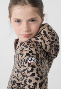 Beige donzen jas met luipaardprint, voorzien van een capuchon en een ronde logopatch op de linker mouw. Gladde textuur.