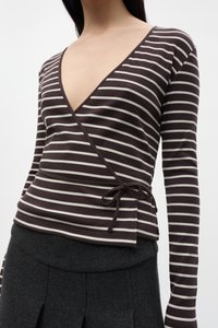 Bruin en crème gestreepte wikkeltop met een diepe V-hals, lange mouwen en een gestrikt zijdetail. Geribbelde textuur. Gecombineerd met een donkere rok.