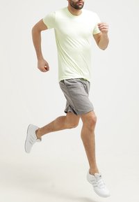 Camiseta ajustada de color verde claro combinada con pantalones cortos grises y zapatillas deportivas blancas. La camiseta tiene una tela texturizada y un escote redondo.