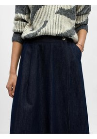 Jupe A-line en denim bleu foncé, dotée d'une taille haute, de plis subtils, de poches latérales et d'une fermeture à bouton métallique avec une finition brillante.