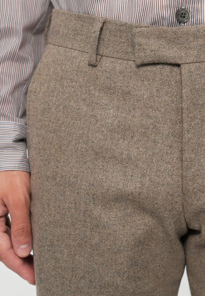 Pantalon en laine texturée marron avec une finition lisse, doté d'un devant plat, de passants de ceinture et d'une coupe ajustée. Chemise rayée visible au-dessus.