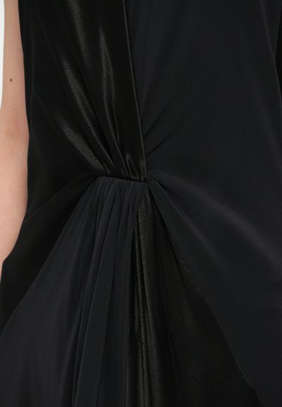 Čierne šaty s detailom uzla v páse, kombinujúce hladkú a štruktúrovanú tkaninu s drapériou pre elegantnú siluetu.