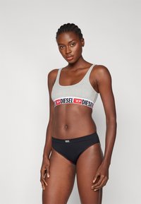 Sivá bavlnená bralette s červeným a čiernym pásom s logom Diesel; kombinovaná s čiernymi nohavičkami s vysokým pásom, ktoré majú malé biele logo Diesel.