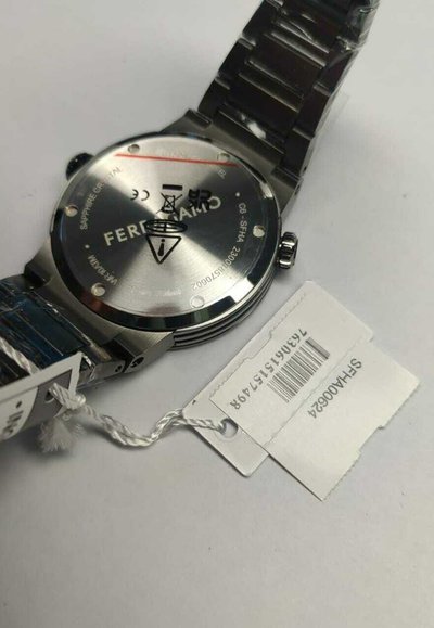 Reloj de acero inoxidable con un acabado plateado pulido, caja redonda y pulsera de metal. Incluye una etiqueta de precio y una cubierta protectora transparente.