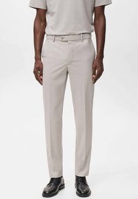 Pantalones de sastre beige con una textura suave, con un lazo para el cinturón y un cierre de botón. Combinados con zapatos de vestir negros.