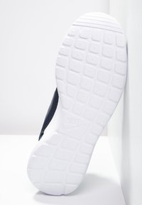 Schwarze Sneaker-Sohle, strukturiertes Gummi mit einem erhöhten Rautenmuster, mit einem großen weißen Nike-Logo. Der seitliche Rand zeigt das marineblaue Obermaterial.