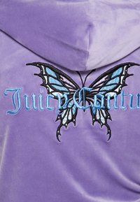 Lavendelvelourhoodie med stor svart, blå och lila fjärilsbroderi samt "JuicyCouture" i blå text.