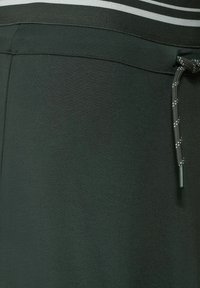 Mørkegrønne atletiksshorts lavet af glat stof, med et bredt elastisk livbånd med hvide striber og en snoretræk til justering.