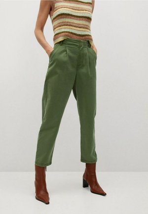 Personne portant un pantalon taille haute vert olive, des bottines marron à talons et un top en maille sans manches avec des rayures beige, marron et vertes.