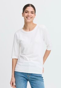 Vit stickad topp med korta ärmar och rund halsringning, med en slät yta och ribbad nederkant, i kombination med ljusblå jeans.