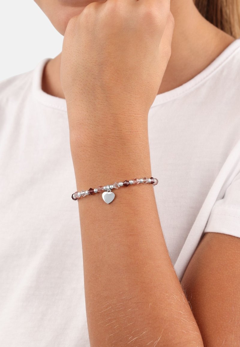 Perlenarmband mit rosa und klaren Perlen, verziert mit einem silbernen Herzanhänger. Am Handgelenk getragen, auf dem die leichte Hautstruktur sichtbar ist.