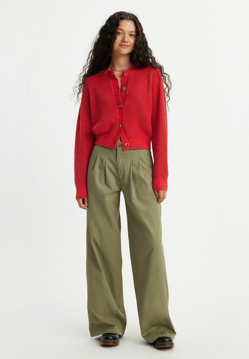 Cardigan rouge à côtes avec un col rond et des boutons devant, associé à un pantalon ample vert olive et des chaussures à plateforme noires.