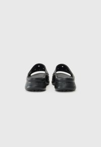 Chaussures noires de style sabot avec un design découpé, en matériau en caoutchouc texturé, et de forme sans dos. Logo de marque proéminent sur le talon. Surface lisse.