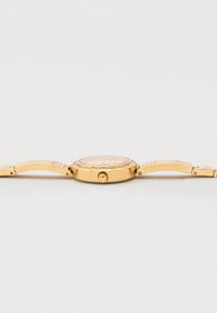 Gold-tone watch with a round face, patterned bezel, textured strap, and an intricate design on the casing. Features a round crown.