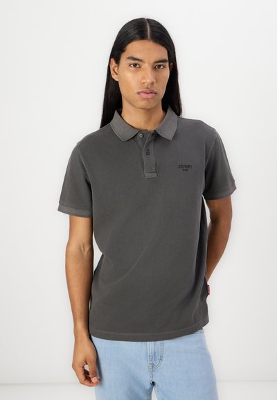 Polo shirt gris foncé avec un col et un plastron à deux boutons. Marquage notable sur la poitrine et manches courtes. Le tissu semble lisse et décontracté.