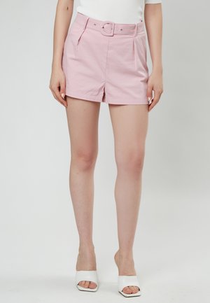 Los pantalones cortos de algodón rosa cuentan con un cinturón con una hebilla rectangular, un diseño de frente plisado y se combinan con sandalias de tacón abiertas blancas.