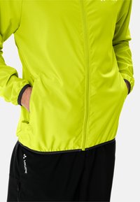 Hellgrüne, leichte Jacke mit Reißverschluss vorne, elastischen Bündchen und zwei Seitentaschen. Schwarze Akzente am Saum und Branding-Detail.