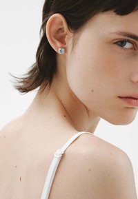 Pendiente de plata con una piedra preciosa azul en forma de cuadrado. Diseño minimalista con textura suave y acabado pulido.