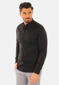 Maglietta nera a maniche lunghe con colletto alto, design aderente e chiusura a bottoni. Texture liscia, tessuto semplice senza motivi o dettagli aggiuntivi.