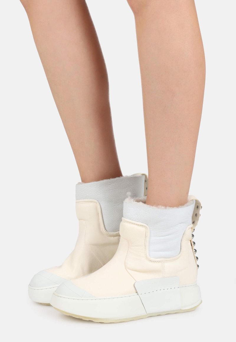 Vita läderankelboots med en texturerad vit krage, som har silvernitar och en gummisula. Den texturerade ytan tillför visuellt intresse.