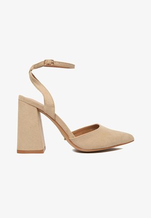 Beige Damenpumps aus Wildleder mit Blockabsatz, spitzer Zehenpartie und verstellbarem Knöchelriemen mit Schnalle vor weißem Hintergrund.