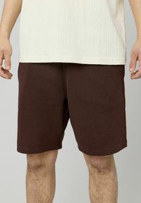 Shorts en coton marron avec une taille élastique, arrivant mi-cuisse, présentant une texture lisse et un design minimaliste.