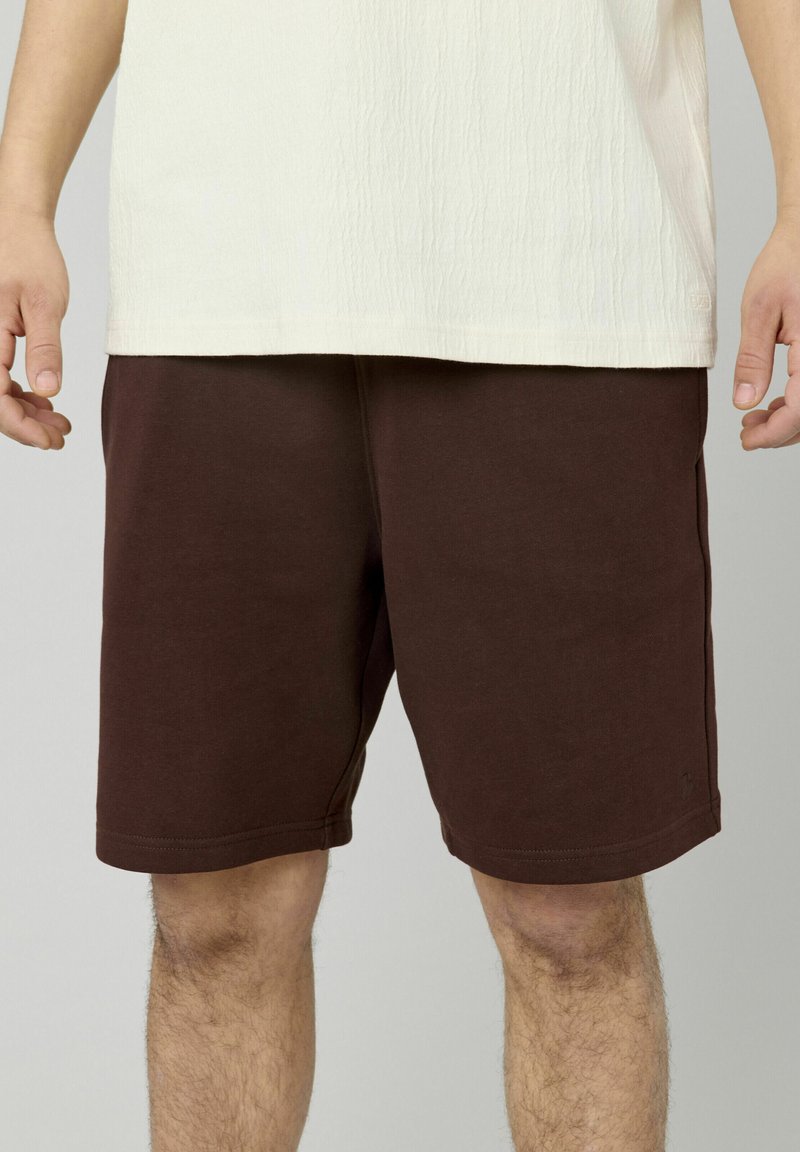Shorts en coton marron avec une taille élastique, arrivant mi-cuisse, présentant une texture lisse et un design minimaliste.