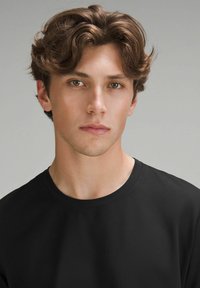 Tricou negru cu guler rotund, din material de bumbac, textură netedă, design ajustat, model cu păr scurt ondulat și fundal neutru.