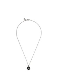 Srebrny naszyjnik z cienkim łańcuszkiem i okrągłym czarnym wisiorkiem z białą literą „C”. Łańcuszek jest cienki, z zapięciem typu karabińczyk.