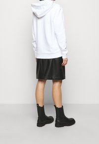 Sudadera blanca con capucha, combinada con una falda corta de cuero sintético negra y botas negras hasta el tobillo. Hardware visible en las botas.
