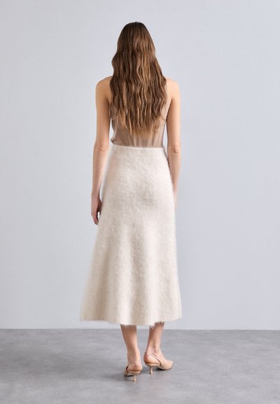 Beige, gulvlængde nederdel lavet af blødt, fuzzy materiale med en flagrende kant. Parret med nude, strop sandaler og en minimalistisk top.