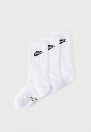 Trois chaussettes blanches Nike mi-mollet avec logos Nike swoosh noirs, disposées en chevauchement sur un fond gris clair.
