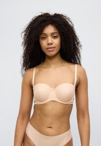 Beige BH med bøyler, glatte, formede kupper, justerbare stropper og en liten sløyfedetalj i midten. Enkel design med delikate sømmer.