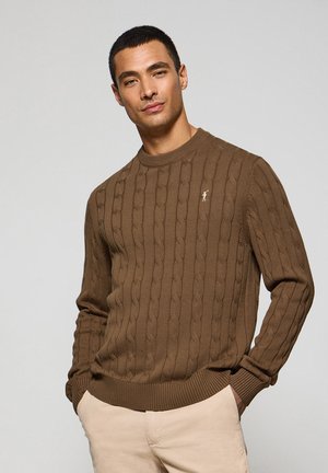 Brauner gestrickter Pullover mit Zopfmuster, geripptem Ausschnitt und Bündchen. Kleines Logoakzent auf der Brust. Leichter Stoff.
